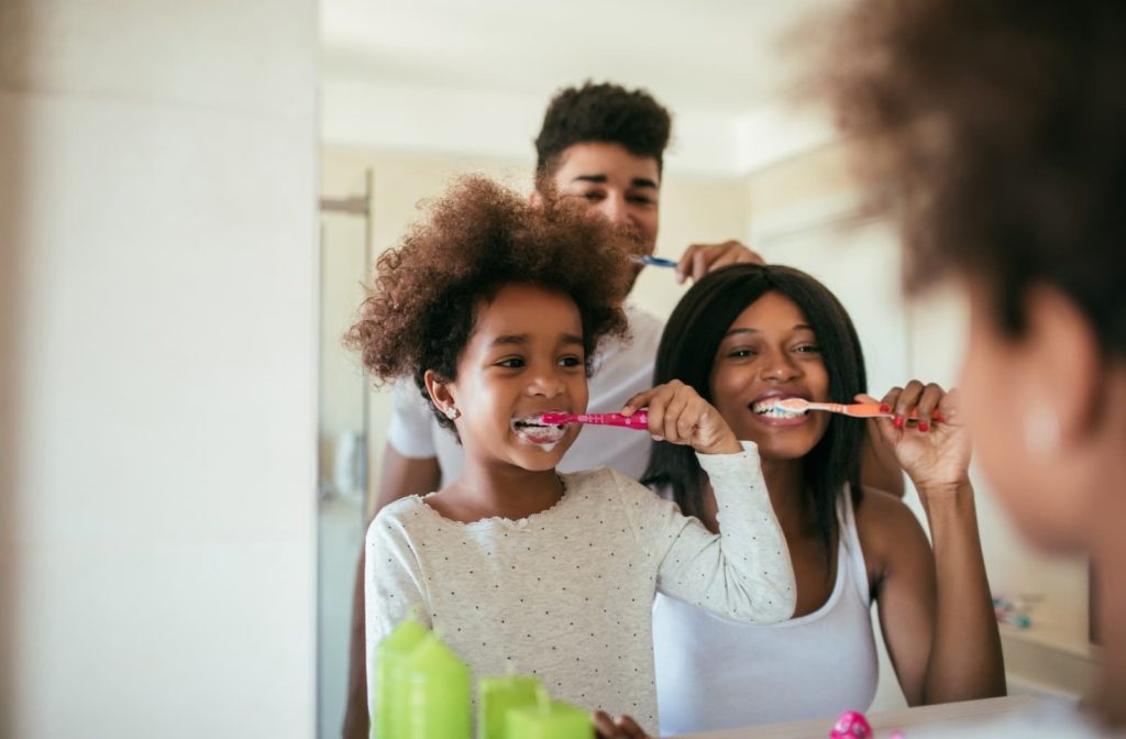 Smiling child, mother, and father brushing their teeth in the mirror