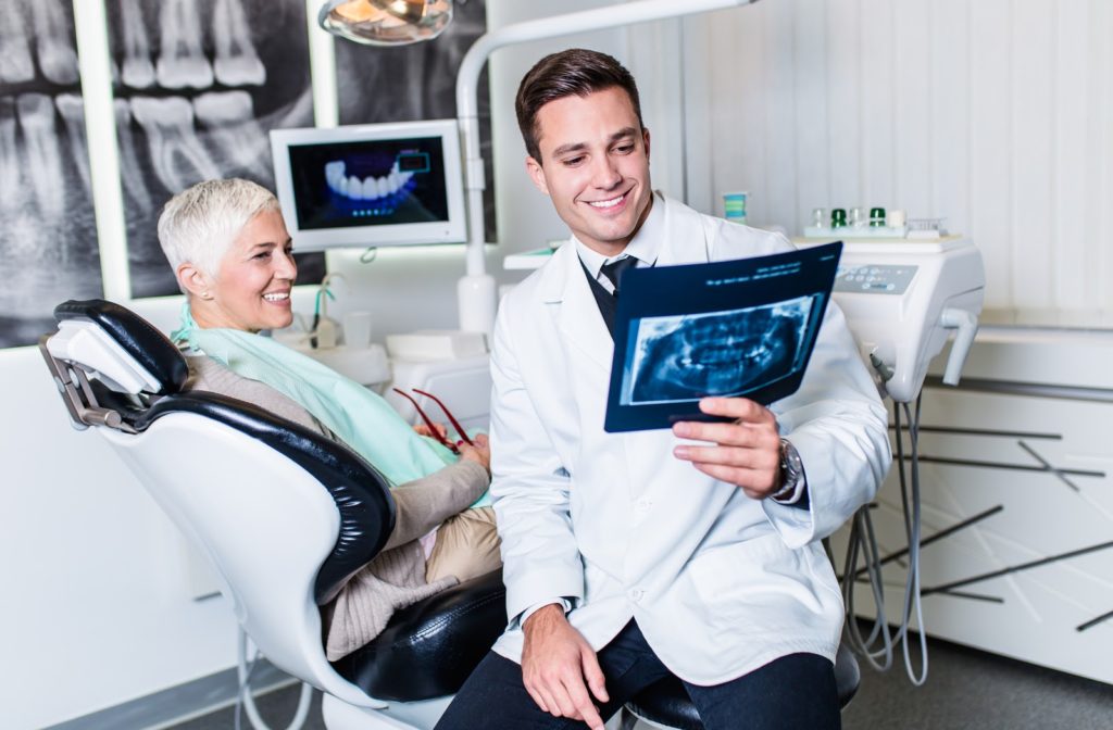 Dentist looking at x-ray of patients tooth as she sits on chair beside him