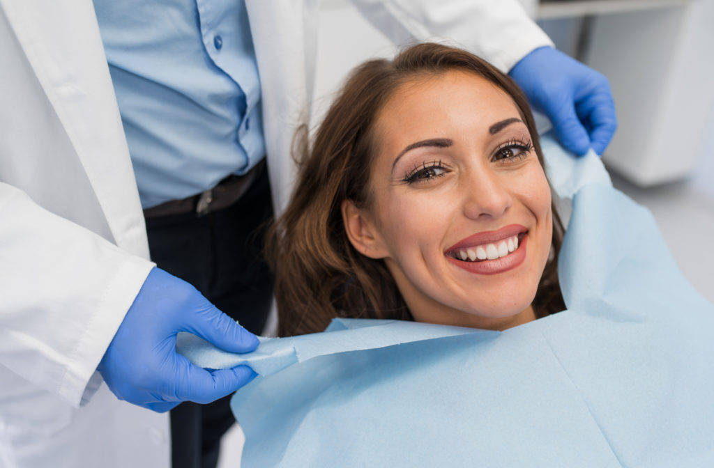 Dentist fixing female patient napkin before undergoing new patient dental exam