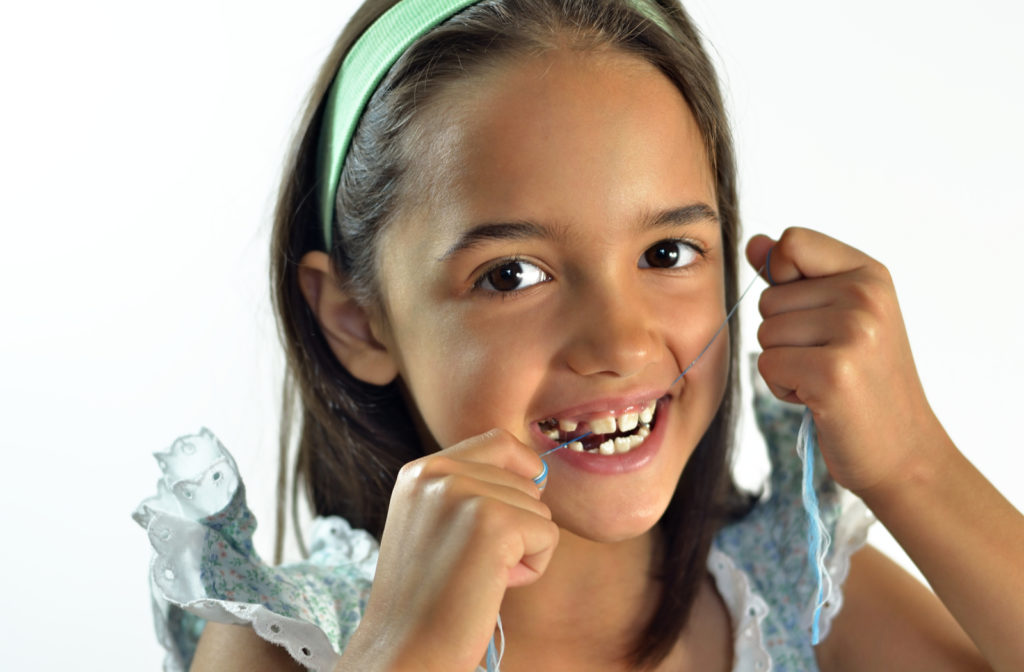 Happy young girl flossing teeth with baby teeth lost