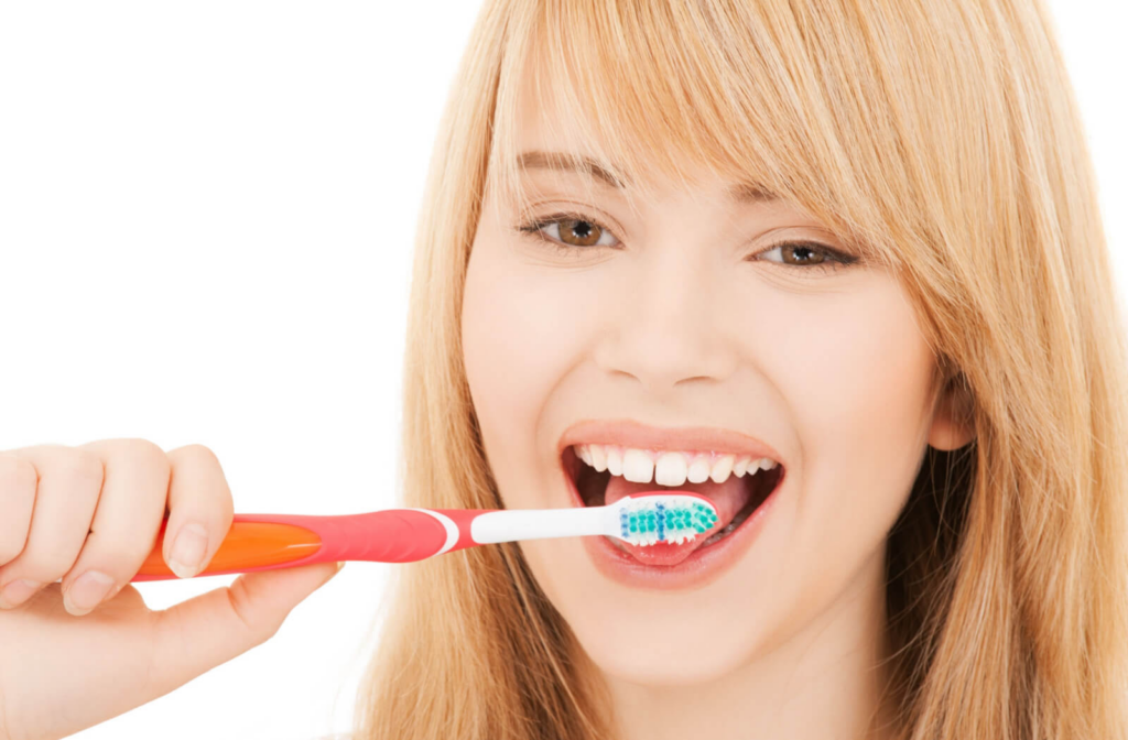 A young woman cleaning her tongue with a toothbrush in her right hand.