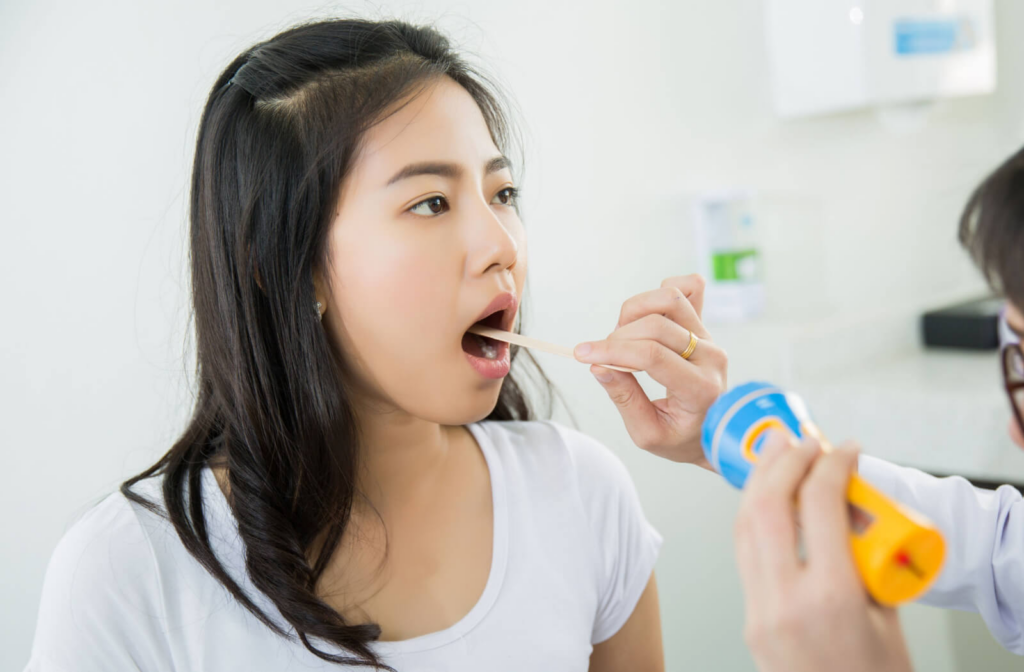 A dentist in a white coat using a tongue depressor to examine a child's mouth