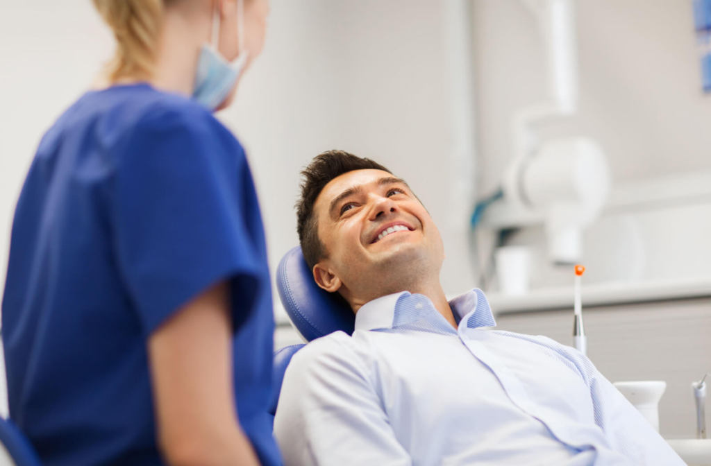 A man sitting in a dentist's chair talking to his female dentist.