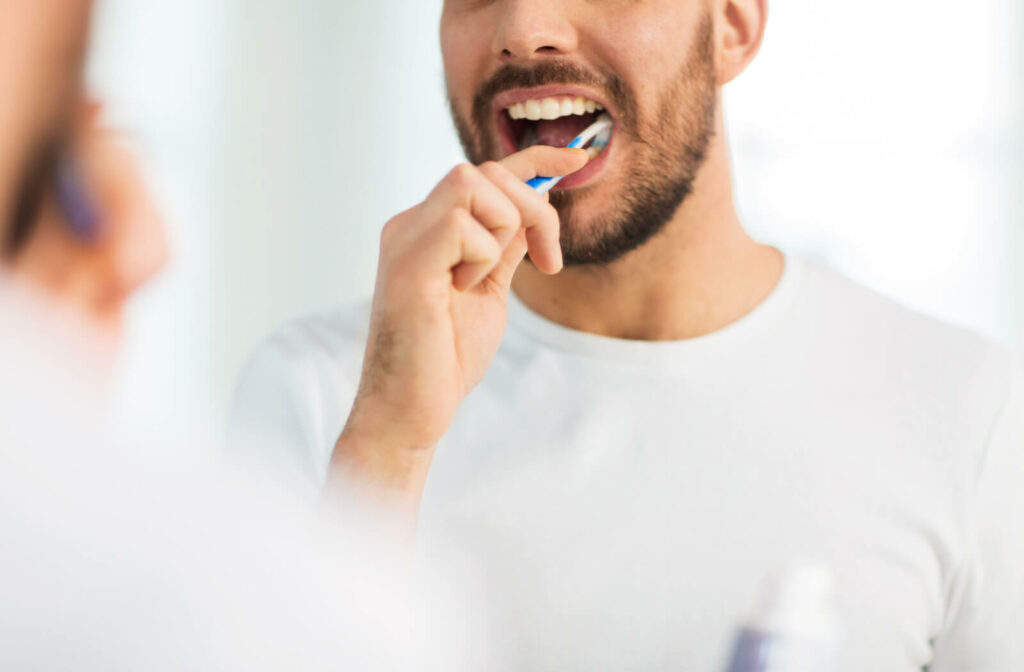 A man in a white t-shirt brushing his bottom teeth with a manual toothbrush