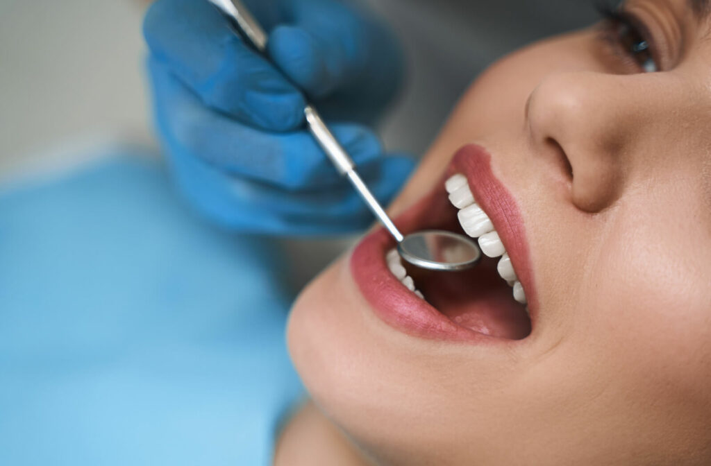 Close-up of woman getting her teeth examined by a dentist with a small mirror