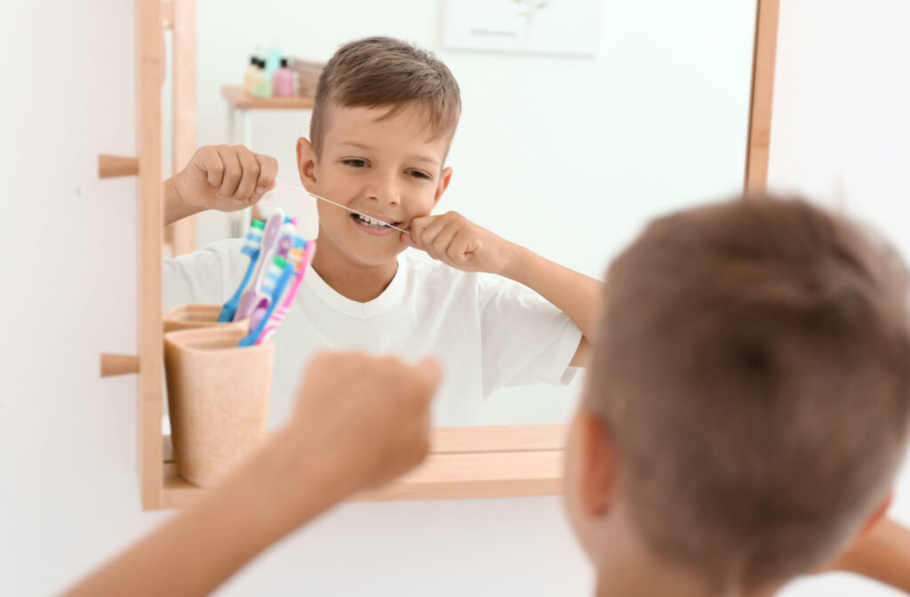 A boy flossing his teeth in front of a mirror in the bathroom.