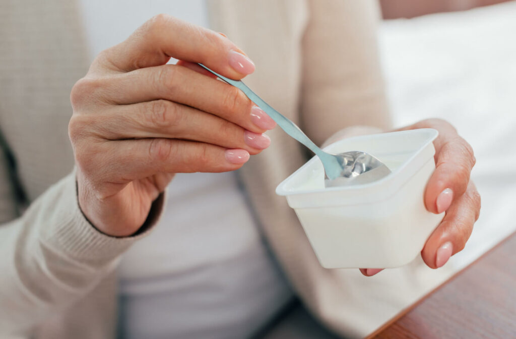 With a spoon in hand, the woman gingerly scoops yogurt, savoring the cool and soothing bites as she enjoys a gentle post-wisdom tooth extraction treat.