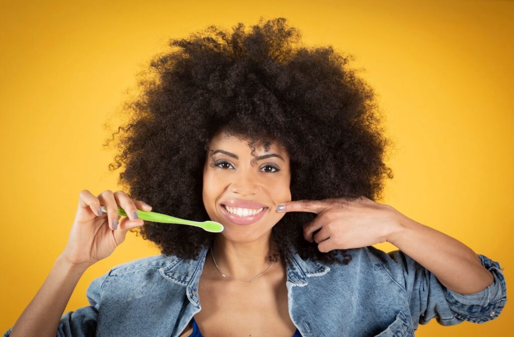 Smiling woman holding a toothbrush and pointing to her mouth, highlighting the importance of good oral hygiene for reducing shifting.