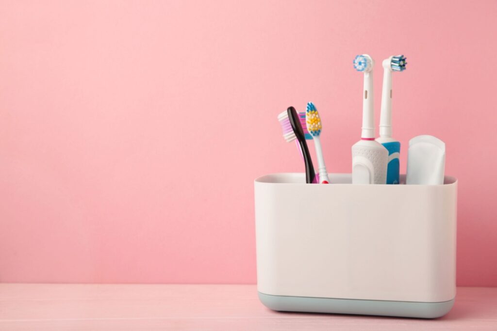 White toothbrush caddy on pink background holding multiple toothbrushes including manual and electric options for family bathroom organization and daily oral care routine.